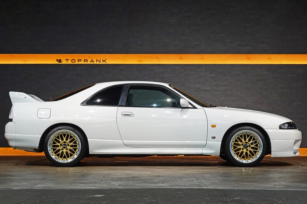 White Nissan Skyline GT-R R33 in profile at a TOPRANK showroom